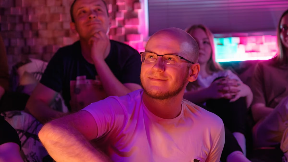 Bald man with eyeglasses and friends enjoying colorful neon atmosphere indoors.